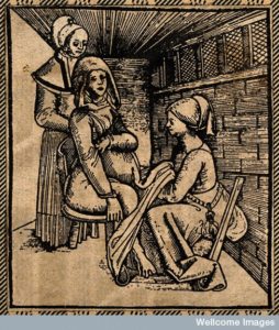 A woman sits in a chair to give birth, supported from behind by a standing woman.  A midwife sits on a stool in front of the woman.